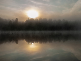 Fototapeta na wymiar Foggy and mystical lake landscape before sunrise. All silhouettes are blurry and unclear. Vaidavas lake, Latvia