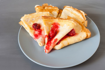 Several stacked pancakes with raspberry jam on a gray plate on a gray textural background