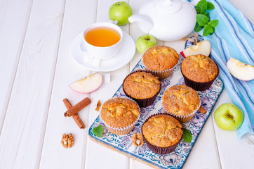 Homemade crispy apple muffins with walnuts and cinnamon on a white wooden background.