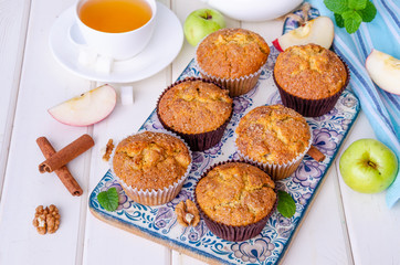 Homemade crispy apple muffins with walnuts and cinnamon on a white wooden background.