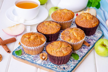 Homemade crispy apple muffins with walnuts and cinnamon on a white wooden background.