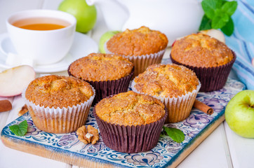 Homemade crispy apple muffins with walnuts and cinnamon on a white wooden background.