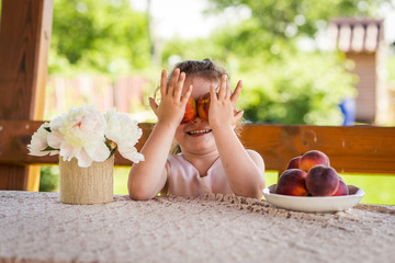 little girl at the table with peaches on nature in summer