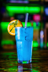 Blue cocktail in a high glass glass with a slice of orange. Colourful cocktail on the dark back. Cocktail on a Colourful  background in a tall glass.