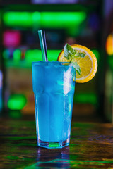 Blue cocktail in a high glass glass with a slice of orange. Colourful cocktail on the dark back. Cocktail on a Colourful  background in a tall glass.
