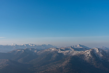 Fototapeta premium Panoramic view of beautiful mountain landscape, snowy mountain peaks covered by forest with a dark blue clear sky background in spring time sunny day