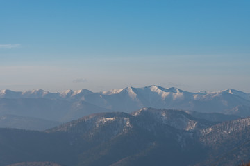 Panoramic view of beautiful mountain landscape, snowy mountain peaks covered by forest with a dark blue clear sky background in spring time sunny day