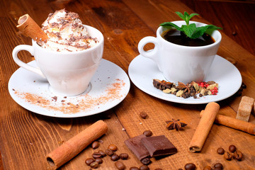 two cups of coffee, grains of coffee, cinnamon scattered on a wooden table.