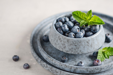 Ripe sweet blueberries in blue bowl on a gray concrete background.