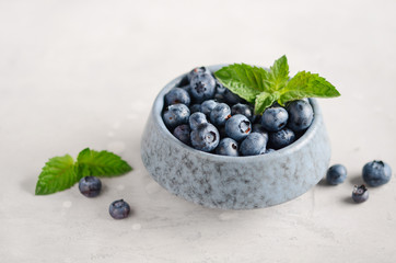 Ripe sweet blueberries in blue bowl on a gray concrete background.