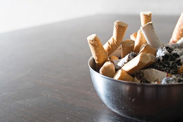 Ashtray full of cigarettes butts close-up on wood background
