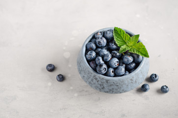 Ripe sweet blueberries in blue bowl on a gray concrete background.