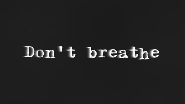 A scary text, Don't Breathe, appearing on the screen with a light behind the typewriter font, typical of a horror flick (b-movie).