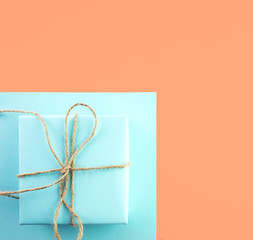 Gift of blue color tied with twine on orange background, top view, minimal styled.