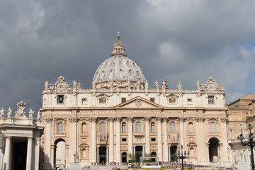 Main facade and dome of Saint Peter's Basilica seen from Saint Peter's Square with rainy clouds on background, Vatican city state, Italy.