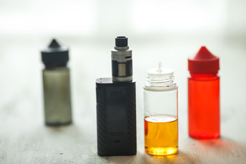 Vape objects. Electronic cigarette and jars with e-liquid on a light wooden table.