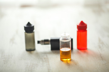 Vape objects. Electronic cigarette and jars with e-liquid on a light wooden table.