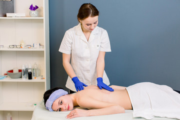 Obraz na płótnie Canvas Ready for massage - oil pouring on woman's back in spa wellness center. Professional body massage to beautiful girl in cosmetology cabinet or beauty parlor.