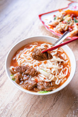 Beef noodle - Taiwan ramen meal with tomato sauce broth in bowl on bright wooden table, famous chinese style food, close up, top view, copy space