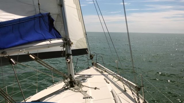 A yacht sailing in light winds, on starboard tack with main and genoa hoisted, on a sunny day in calm coastal waters.