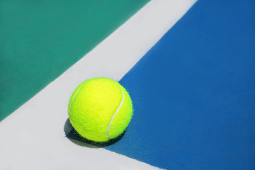 Summer sport concept with tennis ball on white line in the corner of hard tennis court. Flat lay, top view, copy space. Blue and green.