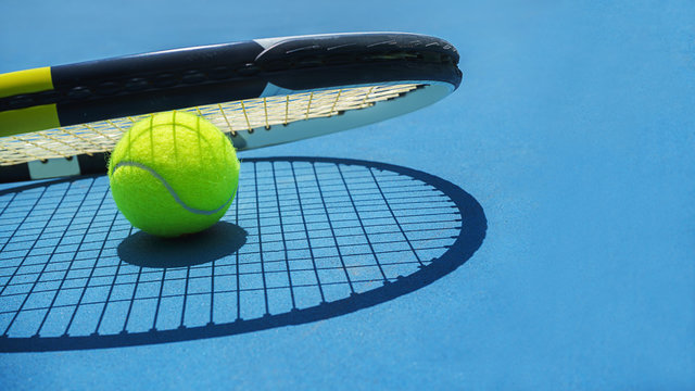 Summer sport concept with tennis ball and racket on blue hard tennis court. Top view, copy space. Blue and yellow. Banner size.