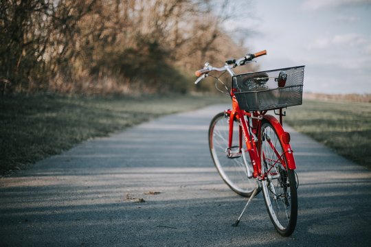 Red Bicycle With A Basket On The Back On A Thin Cement Road In A Field In The Countryside