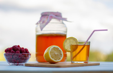 Kombucha  in a jar on a light wooden table against the sky, a glass filled with Kombucha   with raspberries.