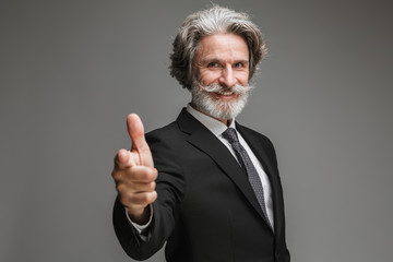 Image of successful adult businessman wearing formal black suit smiling and pointing finger at...