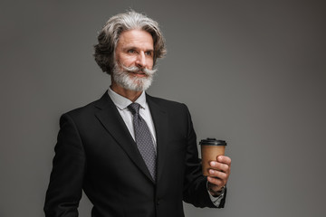 Image of unshaven adult businessman wearing formal black suit smiling and holding paper cup
