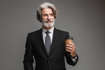 Image of joyful adult businessman wearing formal black suit smiling and holding paper cup