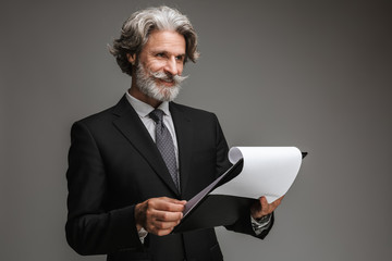 Image of mustached adult businessman wearing formal black suit smiling and holding paper charts