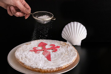 Woman pouring sugar for decorated Tarta de  Santiago or St. James cake, famous spanish almond cake