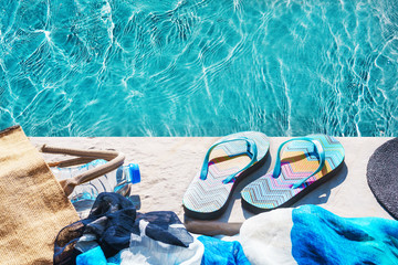 Swimming pool and straw hat, colorful flip flops, wicker bag, straw hat, bottle with still water as...