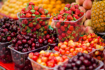 Containers with different ripe berries and fruit at market