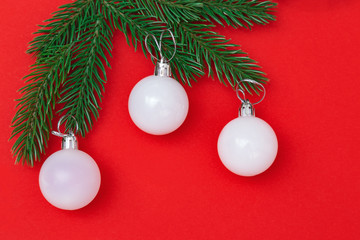 Three White christmas glass balls on green branches over red background. New Year eve decoration. Winter Holiday background with copy space. Flat lay. Top View.