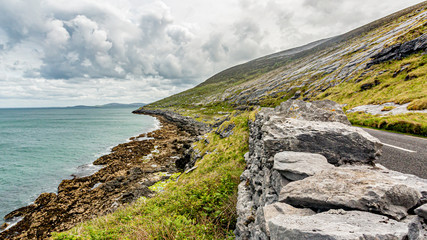 Fototapeta na wymiar Beautiful Irish landscape with the sea and the rural coastal road along​​ the Burren, geosite and geopark, Wild Atlantic Way, cloudy spring day in county Clare, west coastal of Ireland