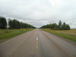 Direct asphalt road through the countryside under the sky, on which the clouds float.