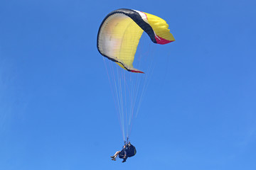 Tandem paraglider flying yellow wing under big ears