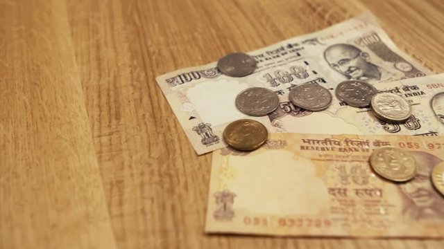 100, 50 and 10 Banknotes of Nepalese Rupee, With Coins Holding the Cash down, on the Wooden table.