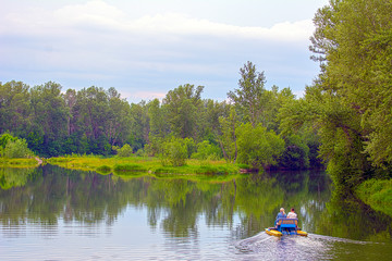 A man and a woman ride on a catamaran on the lake, against the backdrop of the forest
