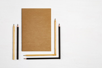 Geometric pencils folded and closed notebook on white desk. Six wooden pencils and book for drawing. Back to school concept. Copy space. Top view.