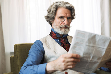 Portrait of attractive adult businessman reading newspaper while sitting on armchair in hotel...