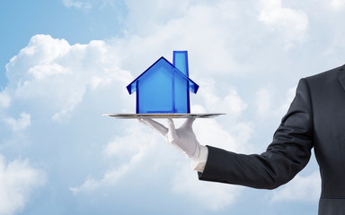 Businessman offering blue crystal house model on silver tray over blue sky 