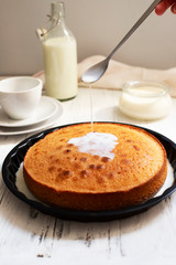 Traditional dessert Three Milk, Tres Leches or Trilece. Served on a white wooden table with milk in a bottle and a cup. Milk pours from a spoon onto a biscuit. Biscuit soaked with milk. Closeup