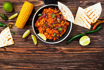 Traditional Mexican chili con carne served on a rustic wooden background in a pan with corn, mexican tortilla bread, lime and jalapeño. Top view. Space for text