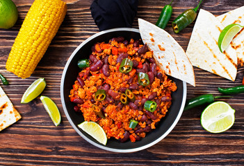 Traditional Mexican chili con carne served on a rustic wooden background in a pan with corn, mexican tortilla bread, lime and jalapeño. Top view. Space for text