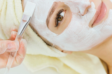 Portrait of beautiful woman laying with towel on the head. Hands of cosmetology specialist applying...