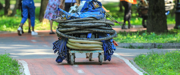 An employee of a city park is carrying a cart with a hose for watering the plants. 