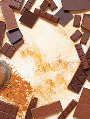 Assortment of different types of chocolate and cocoa powder on a light marble background. Top view, flat lay. Space for text